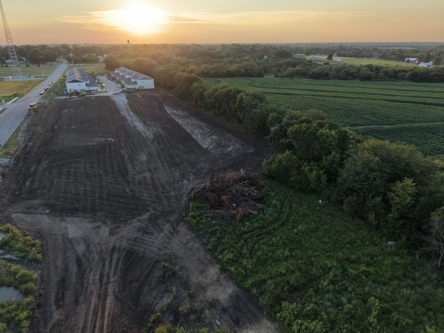 Aerial view at sunset of the graded ICON Valley Phase 2 site in Wellsville, Kansas, with the completed Phase 1 townhomes beyond